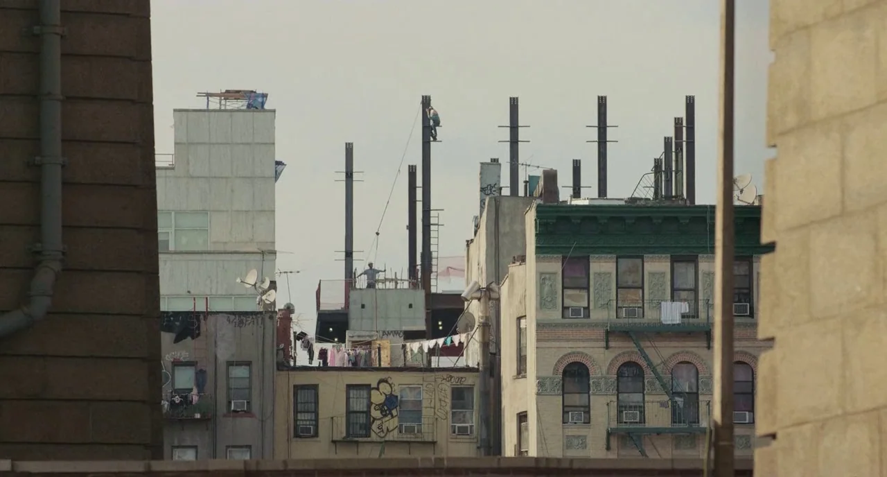 Skate Kitchen (2018) movie still: wide — An urban cluster of apartment buildings features exposed steel construction framing on a rooftop. Workers…