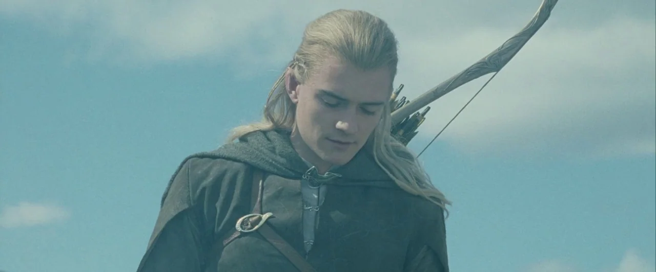 The Lord of The Rings: The Two Towers (2002) movie still: medium — A fair-skinned elf stands outdoors against a bright blue sky filled with clouds.…