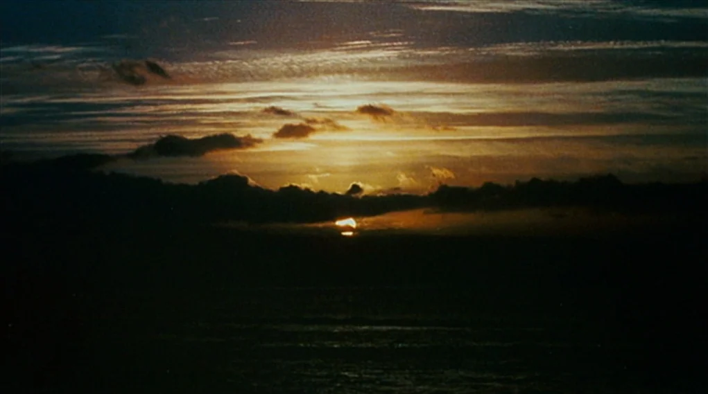 Visioneers (2008) movie still: establishing — A wide view of the sun dipping below the horizon over dark water. Streaks of gold and orange clouds…