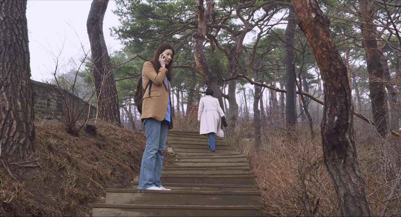 Nobody’s Daughter Haewon (2013) movie still: fullbody — A wooden staircase winds through a sparse, late-winter woodland of pine trees. One woman…