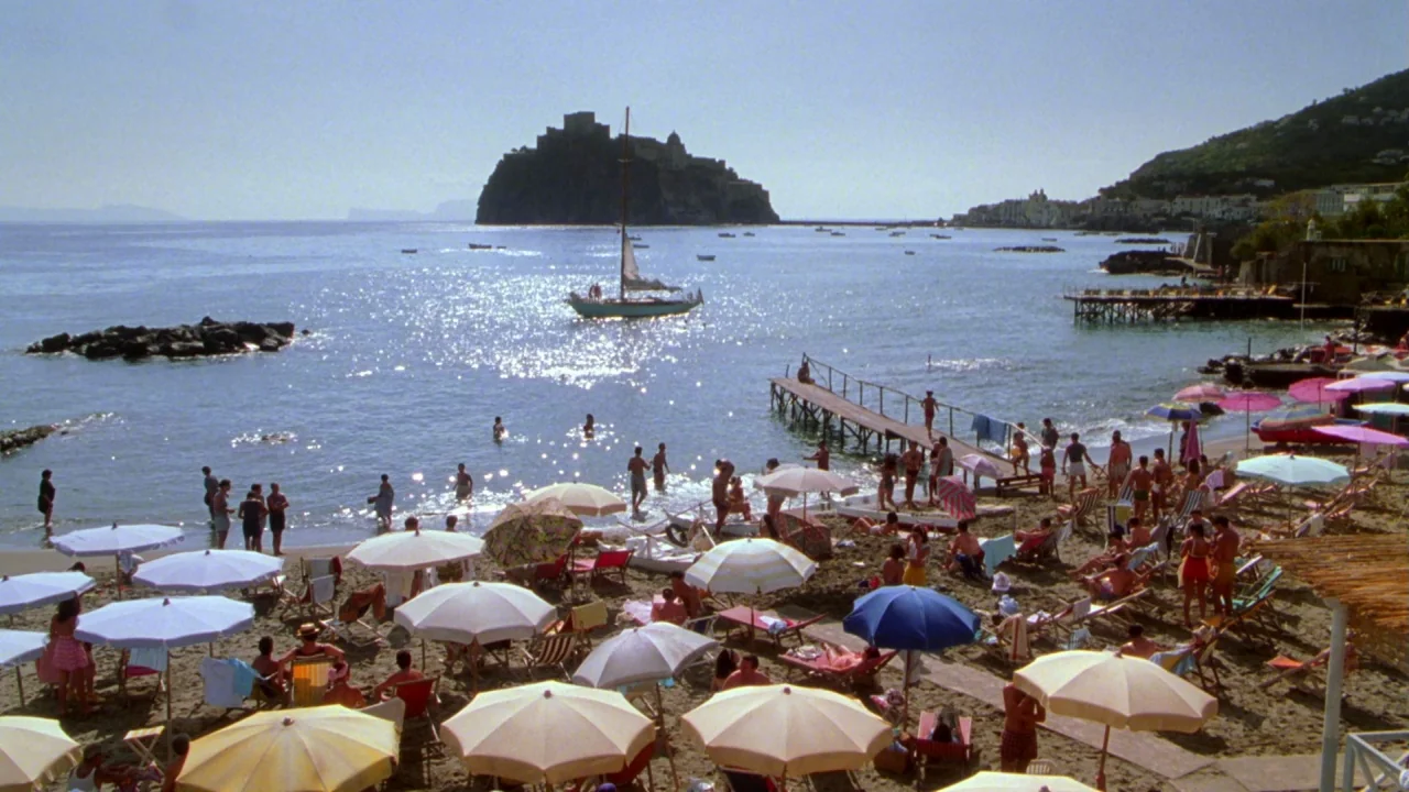 The Talented Mr. Ripley (1999) movie still: establishing — A sunny coastal beach scene features numerous colorful umbrellas and people near the…
