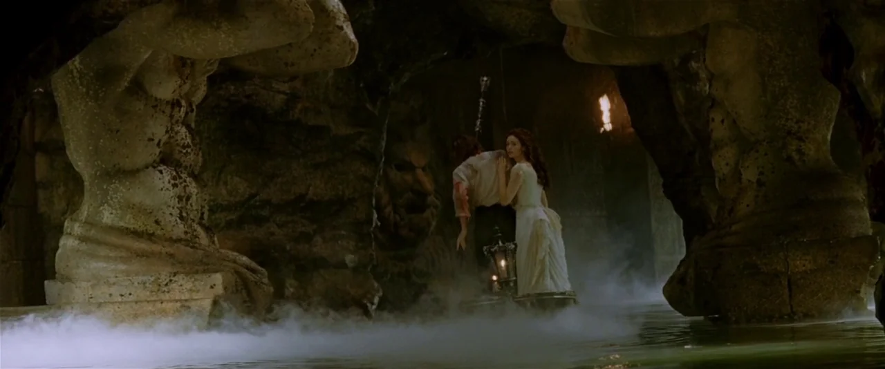 The Phantom of the Opera (2004) movie still: wide — A subterranean limestone grotto features large stone columns carved into figures flanking a…