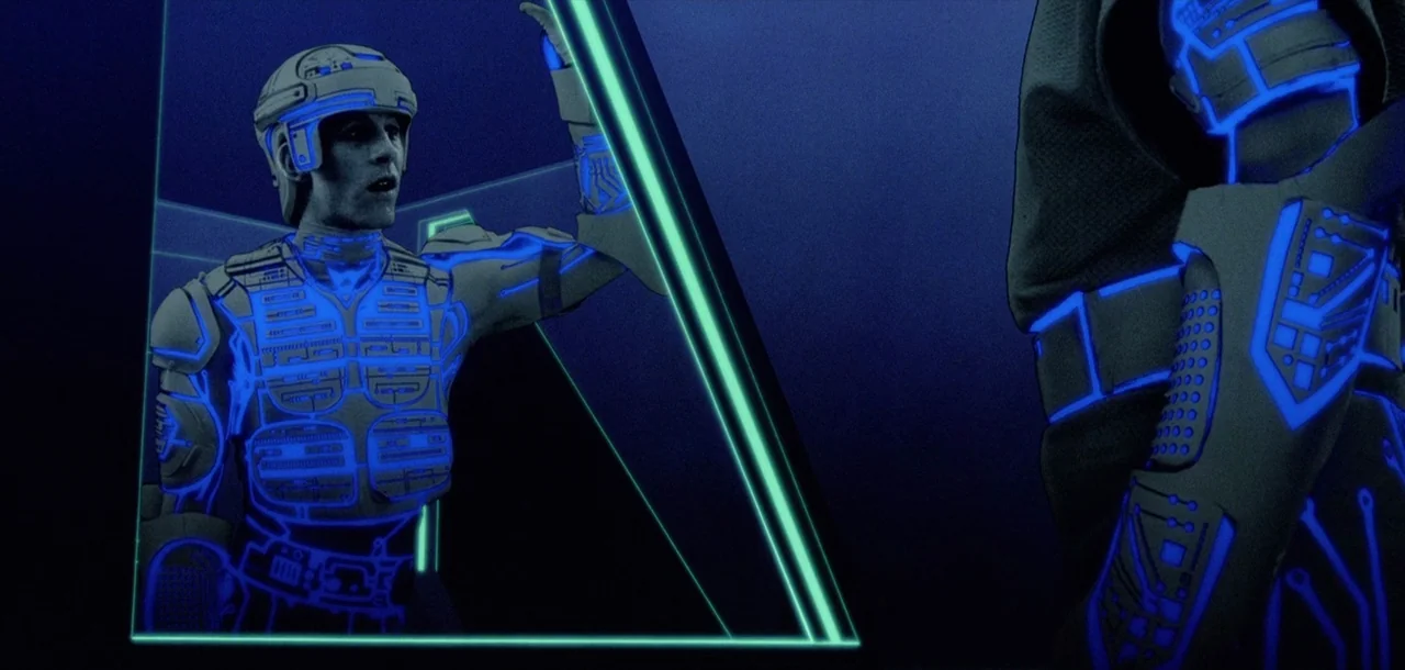 Tron (1982) movie still: medium — A dark digital environment filled with sharp, luminous blue geometric architectural elements. A man in a light-up…