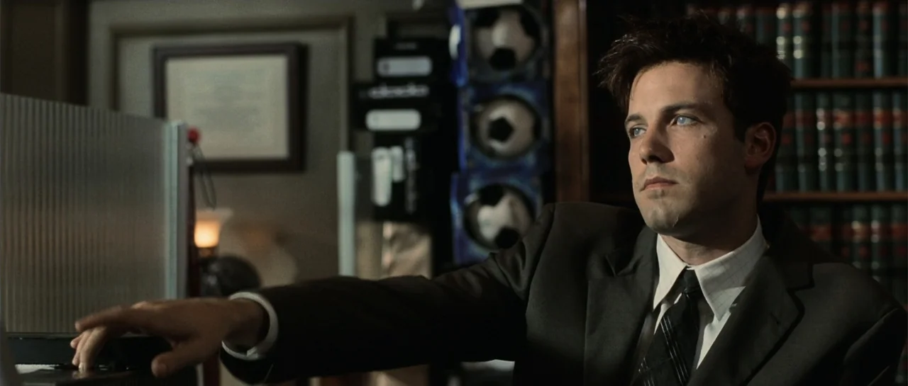 Daredevil (2015) movie still: medium — A dimly lit professional office with a bookshelf filled with volumes behind the subject. A man in a suit sits…