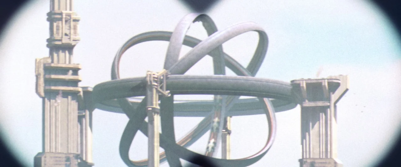 Contact (1997) movie still: establishing — A massive metallic ring structure is mounted between tall futuristic columns in the sky. Viewed as if…
