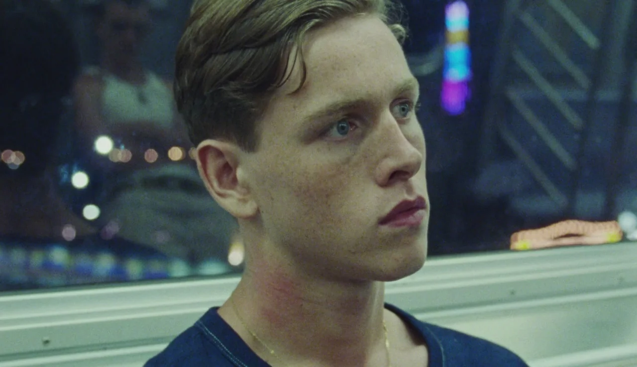 Beach Rats (2017) movie still: closeup — A man sits inside a subway car at night with a city view outside the window. He looks forward with a…