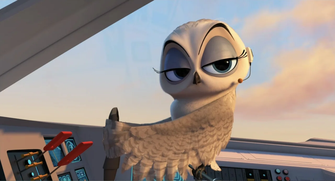Penguins of Madagascar (2014) movie still: medium — A snowy owl wearing a headset sits in the cockpit of an aircraft. The owl rests one wing on the…