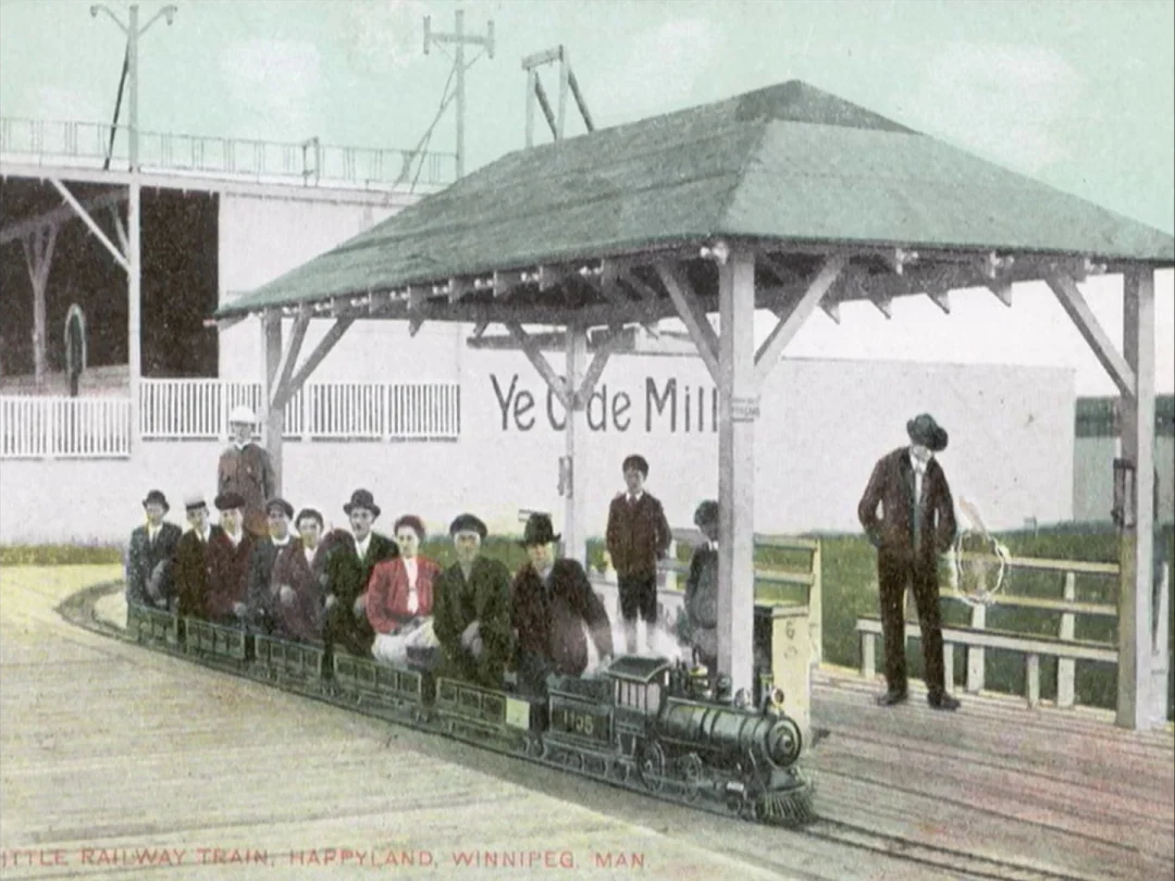 My Winnipeg (2007) movie still: wide — A miniature train sits at a covered station with a wooden roof and floor. A group of people sits in the small…