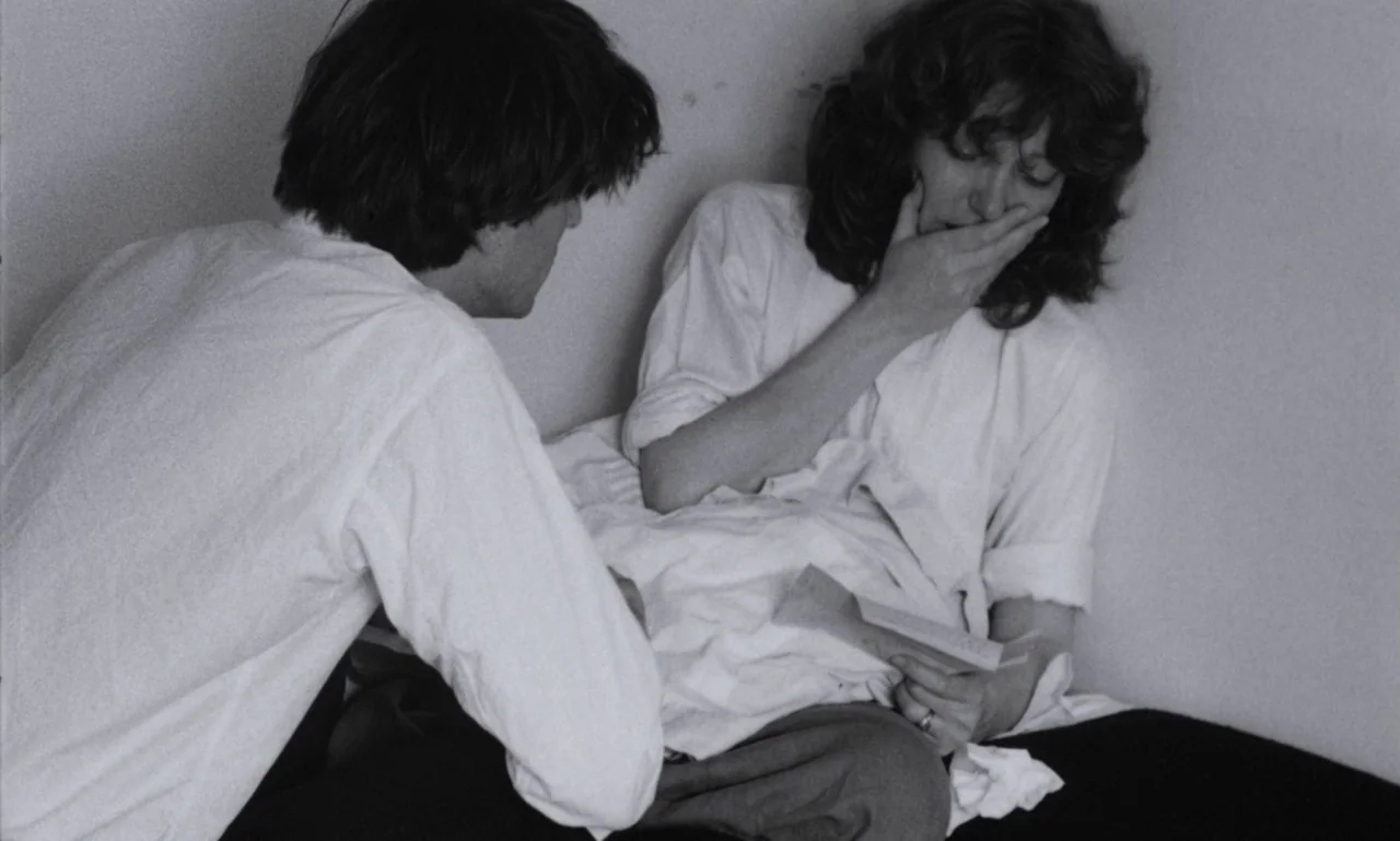 The Secret Son (1979) movie still: medium — A spare interior corner with plain walls and white bedding on the floor. A man sits beside a woman who…