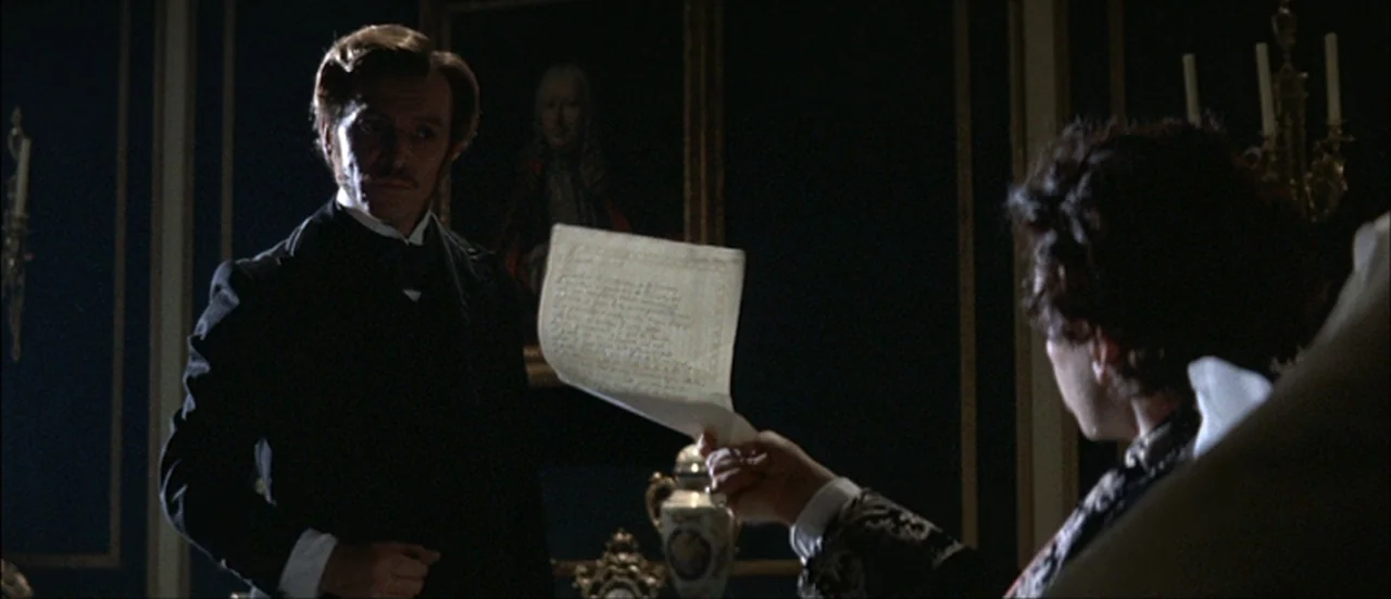 Ludwig (1973) movie still: medium — A dimly lit room features dark blue walls decorated with framed classical oil paintings. A man in a dark suit…