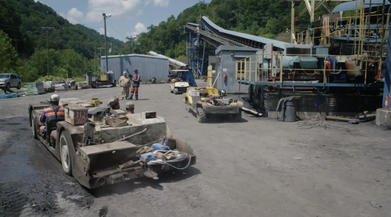 The Divided Soul of America (2019) movie still: wide — A dusty industrial coal mine yard features heavy machinery and a metal conveyor structure. A…