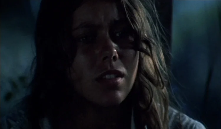 Walkabout (1971) movie still: closeup — A dimly lit interior space characterized by heavy shadows and cool color tones. A young woman with long wavy…