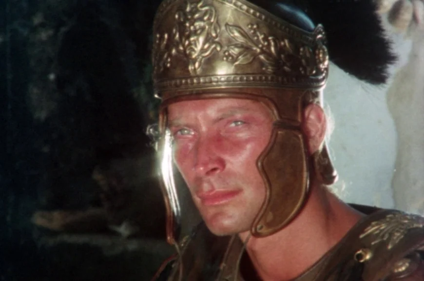 Sebastiane (1976) movie still: closeup — A man in ancient Roman military regalia stands against an out-of-focus natural backdrop. He wears a…