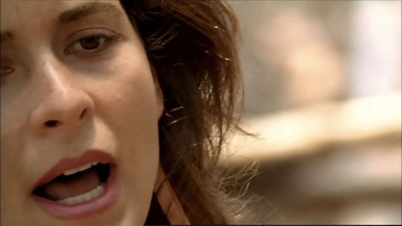 In the Middle of the World (1990) movie still: closeup — The frame shows a closeup of a woman outdoors during the day. She has her mouth slightly…