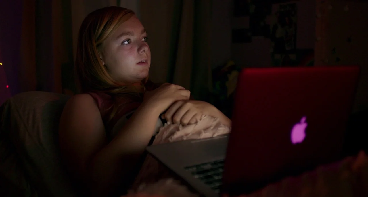 Eighth Grade (2018) movie still: medium — A dimly lit room at night serves as the setting for a late-night activity. A teenager lies in bed watching…