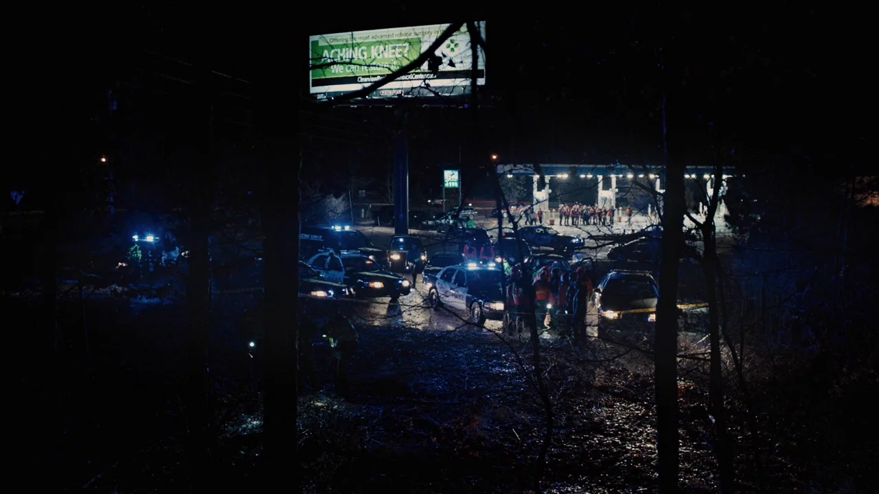 Prisoners (2013) movie still: wide — A nighttime scene features a gas station cordoned off with yellow caution tape. Multiple police vehicles…