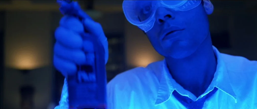 Se7en (1995) movie still: closeup — A dimly lit room illuminated by a pervasive, artificial blue light source. A man wearing laboratory safety…