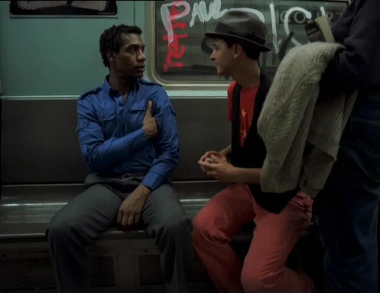 The Brother From Another Planet (1984) movie still: medium — Interior of a subway car featuring graffiti on the window and muted green walls. Two…