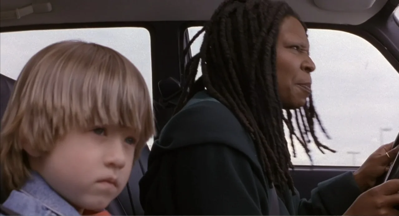 Bogus (1996) movie still: medium — The interior of a moving vehicle with a woman driving and a child passenger. The woman looks ahead while the boy…