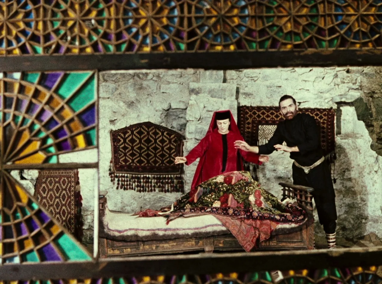 The Colour of Pomegranates (1969) movie still: medium — A stone chamber features rough walls adorned with patterned woven tapestries and carpets. A…