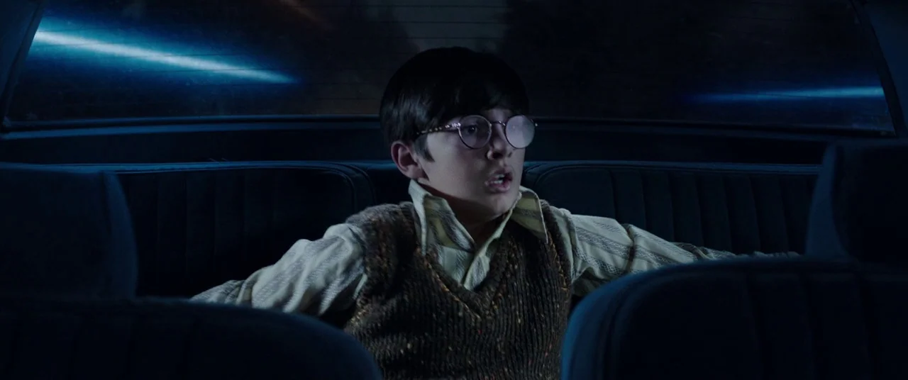 Shazam! (2019) movie still: medium — A dark interior of a car shows a young boy sitting in the backseat. He looks ahead with a wide-eyed expression…