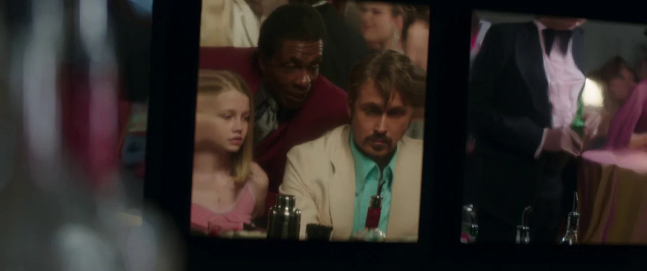 The Nice Guys (2016) movie still: medium — A dimly lit 1970s bar interior with figures visible through glass frames. A man in a cream suit sits next…