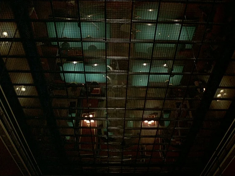 Detective (1985) movie still: establishing — A high-angle view looks down through a metal security grate at a pool hall. Multiple pool tables are…