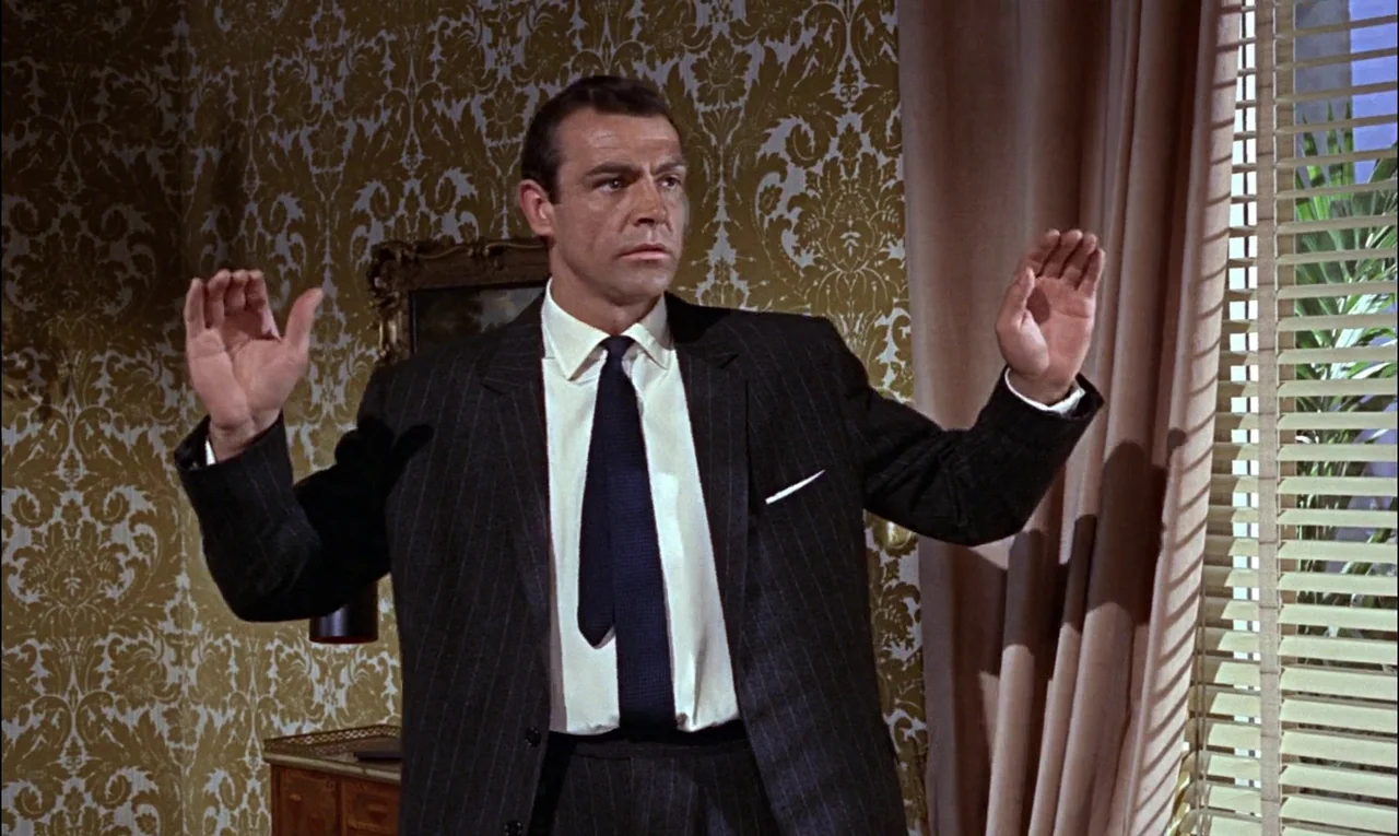 From Russia With Love (1963) movie still: medium — An interior wall covered in ornate gold and white patterned floral wallpaper. A man in a tailored…