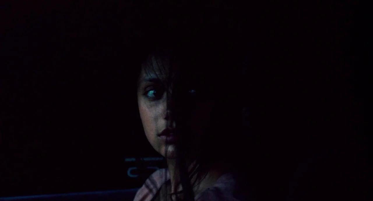 Ava (2017) movie still: closeup — A dark, cramped space inside a vehicle at night with minimal illumination. A woman stares into the darkness while…