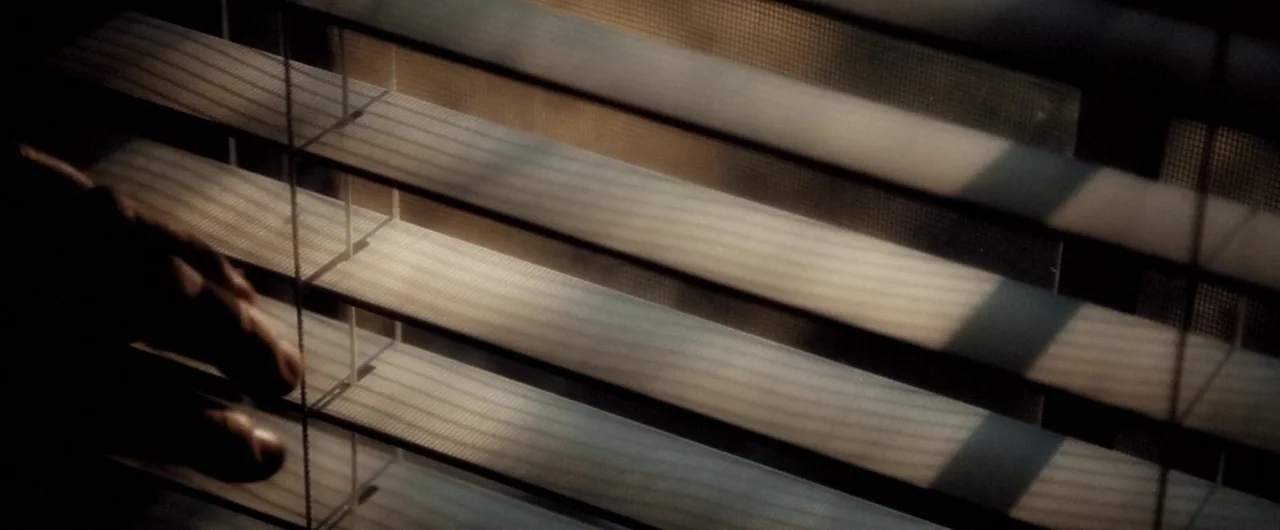 No Man of God (2021) movie still: closeup — Horizontal window blinds are partially tilted to allow narrow shafts of daylight inside. The slats…