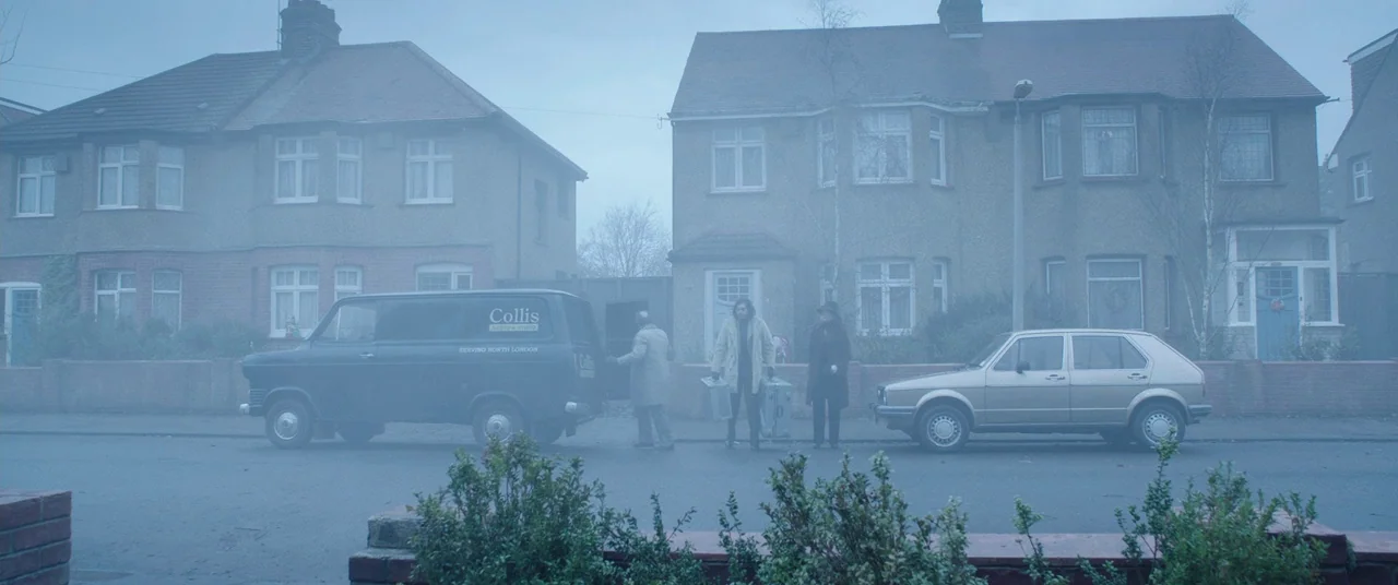The Conjuring 2 (2016) movie still: wide — A quiet residential street lined with semi-detached brick houses is shrouded in light fog. Three men in…