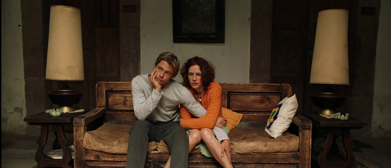 The Mexican (2001) movie still: medium — A rustic wood-paneled wall features two lamps flanking a wooden bench with cushioned seats. The man has his…