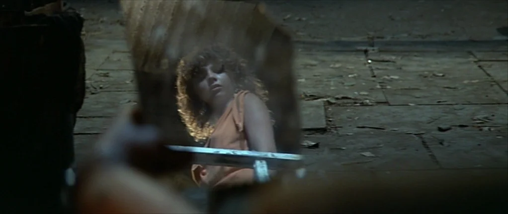 The Moon in the Gutter (1983) movie still: closeup — A dark, dimly lit basement with stone floor tiles and scattered debris. A woman stares at her…