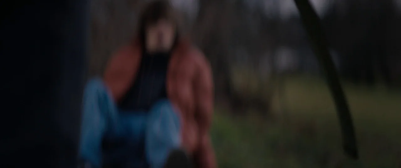Super Dark Times (2017) movie still: medium — An open grassy field at twilight is blurred, focusing on a single figure. A person wearing a puffy…