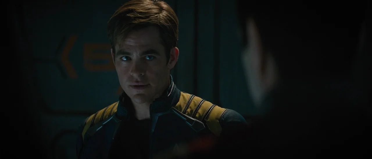 Star Trek Beyond (2016) movie still: closeup — A dimly lit, metallic interior environment with low-contrast surfaces and structural paneling. A man…