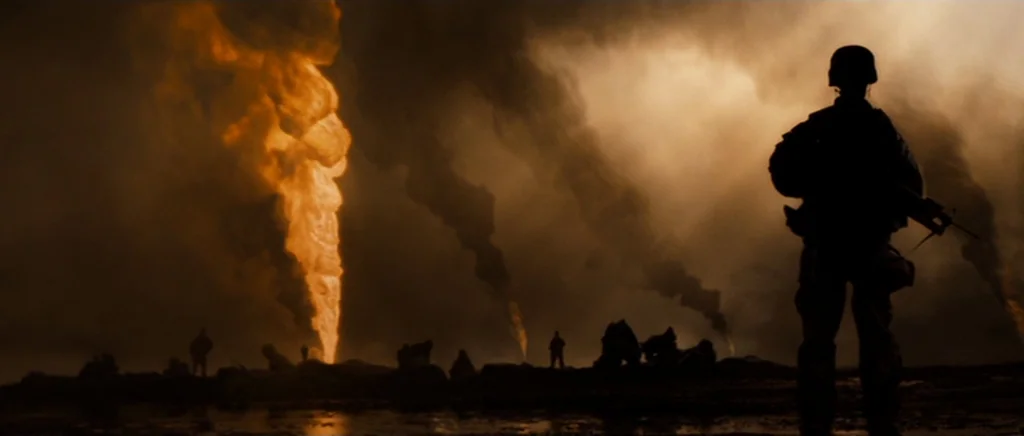 Jarhead movie still: wide — A dark oil field at night filled with thick, billowing black smoke. Soldiers are silhouetted against tall pillars of…