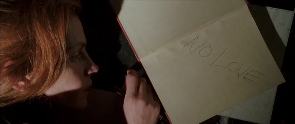 Confessions of a Dangerous Mind (2002) movie still: closeup — A close-up shot focuses on a person lying down near an open book. The text no love is…