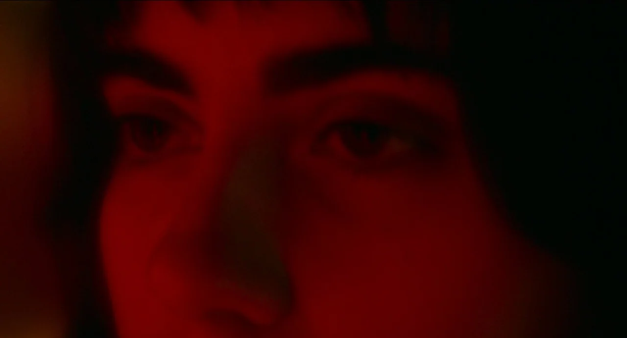 Trim Season (2023) movie still: closeup — A close-up of a person's eyes and nose obscured by deep shadows. The face is entirely lit by a harsh red…