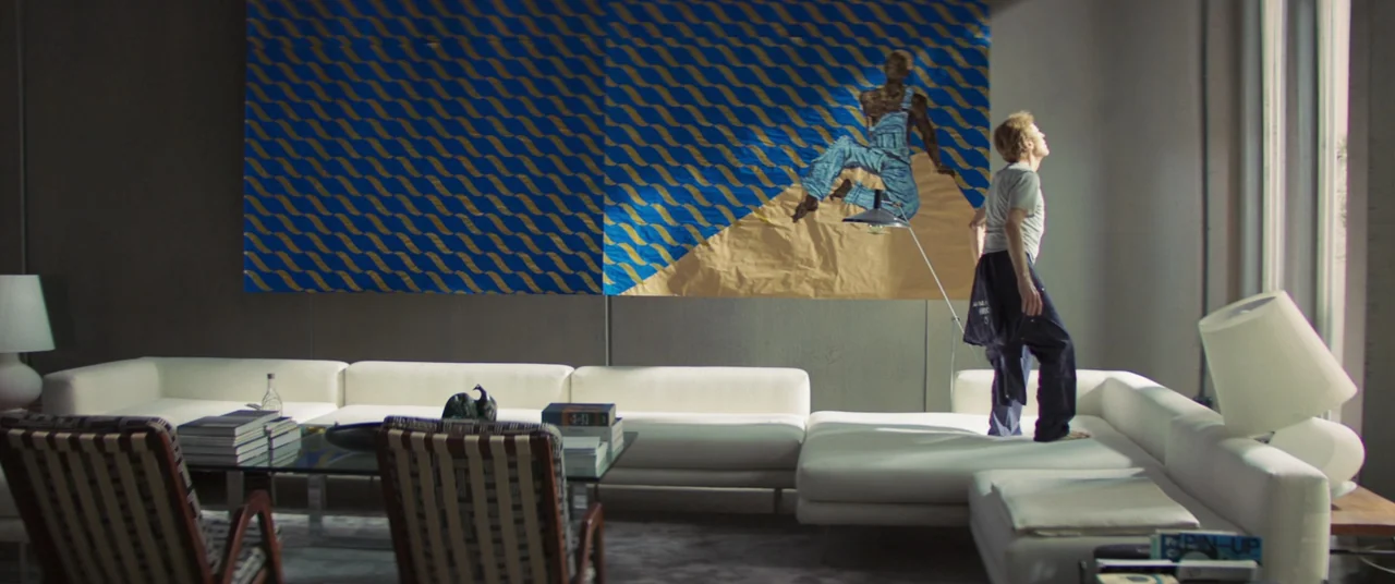 Inside (2023) (2023) movie still: wide — A modern, minimalist living room features a large yellow and blue geometric wall mural. An elderly man…