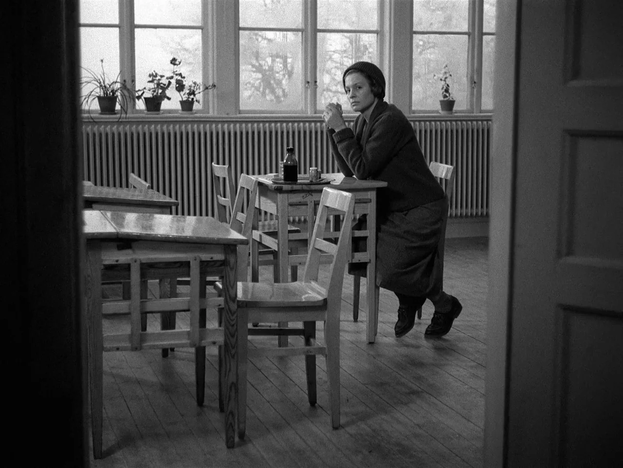 Winter Light (1963) movie still: medium — A classroom features rows of wooden desks and chairs in front of large windows. A woman in a dark sweater…