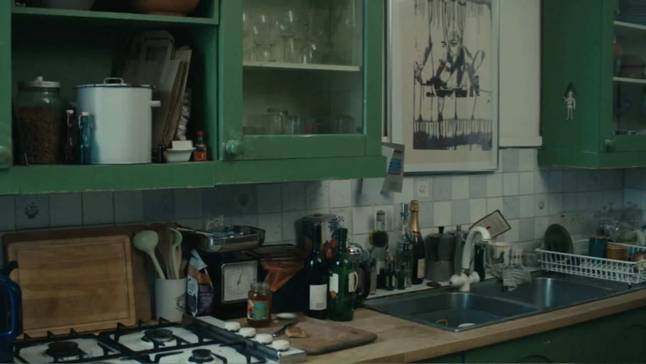 About Time (2013) movie still: medium — A kitchen features green cabinets, tiled backsplash, and a wooden countertop with cookware. Various bottles,…