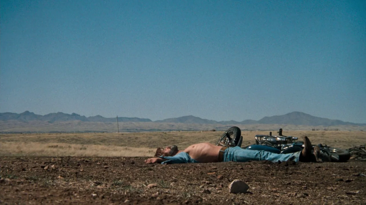 A Star Is Born (1976) movie still: wide — A vast, dry desert landscape stretches toward distant mountains under a clear blue sky. A man lies on the…