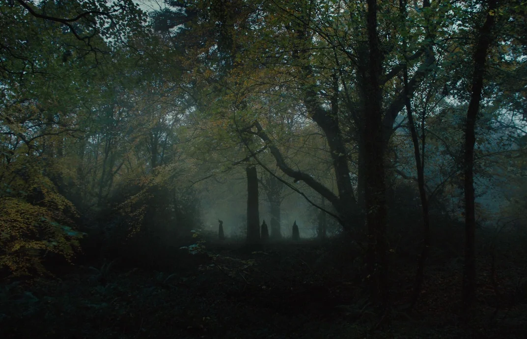 Gretel & Hansel (2020) movie still: wide — A dense, fog-filled woodland area features many tall, slender trees with autumn-toned leaves. Three…
