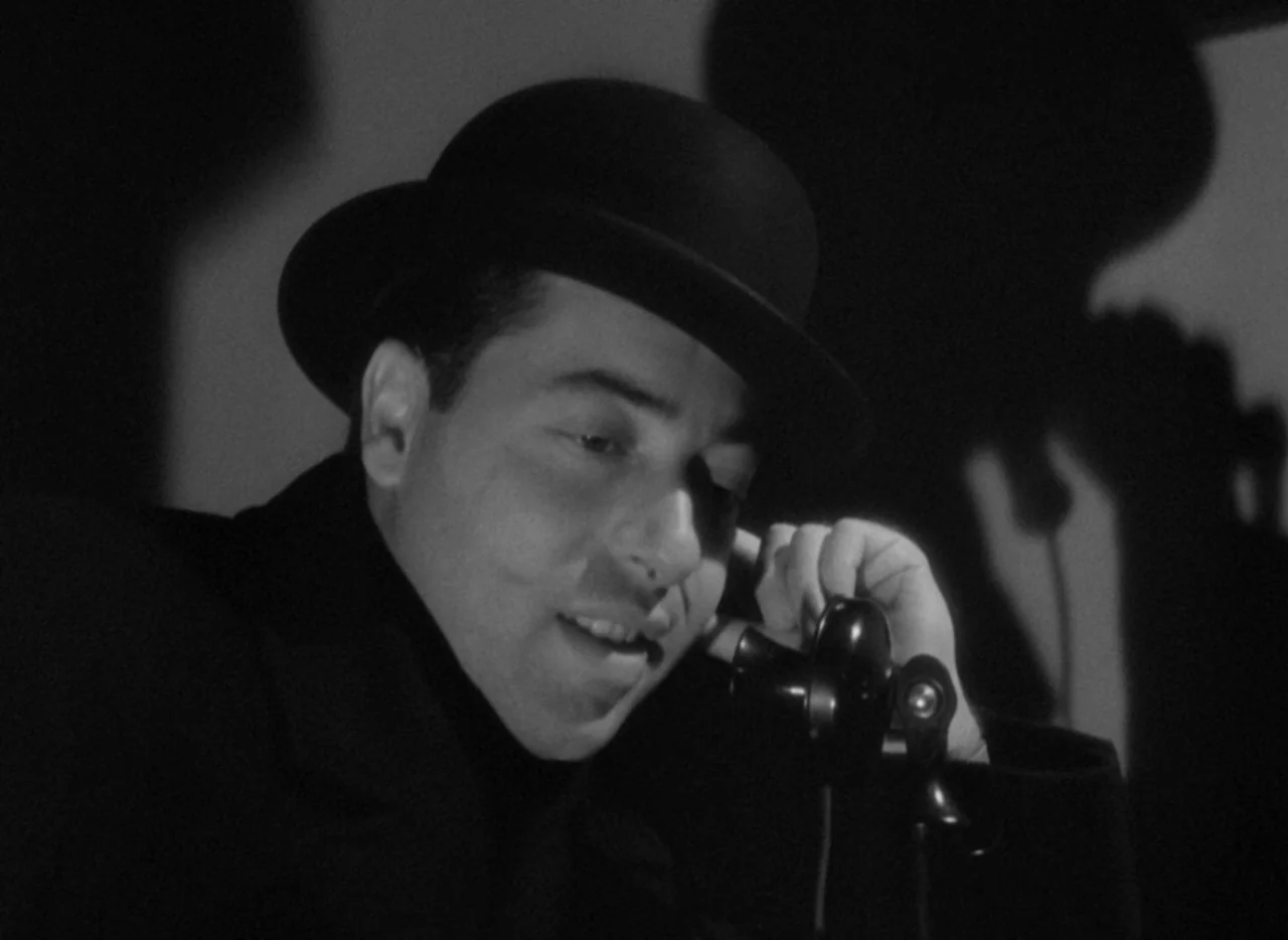 The Thin Man (1934) movie still: closeup — A man wearing a bowler hat speaks into a vintage telephone receiver. A large shadow is cast against the…