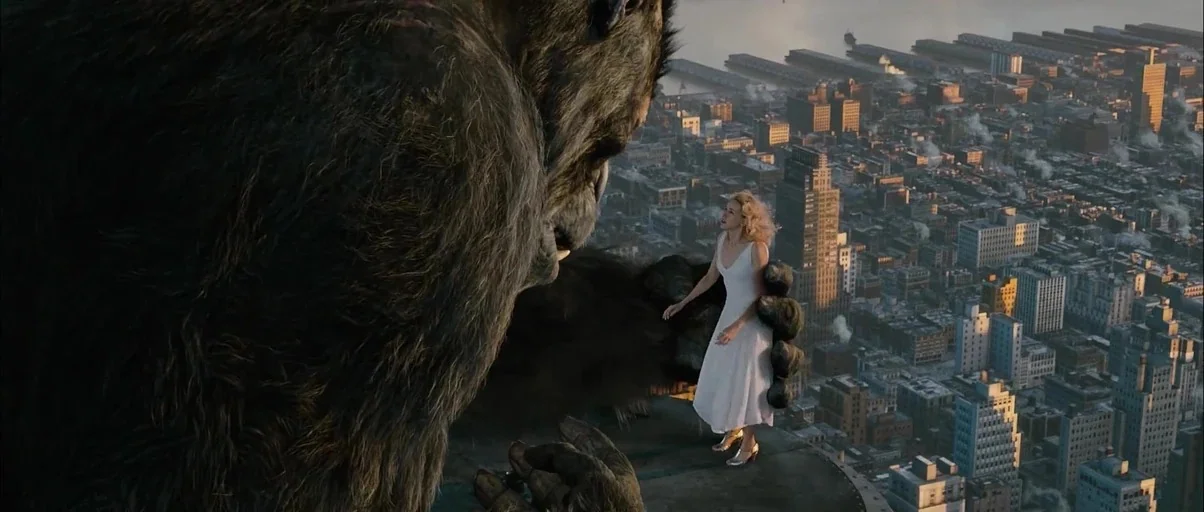 King Kong (2005) movie still: wide — A woman in a white dress stands on the flat roof of a skyscraper. A giant gorilla sits nearby on the structure…