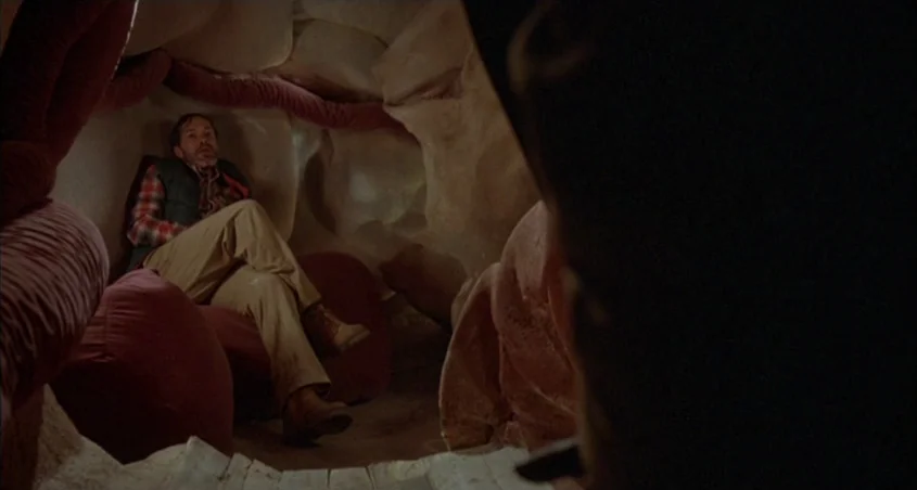 Scanners (1981) movie still: medium — The interior of a large, organic-looking structure constructed from soft, fleshy-toned material. A man sits…