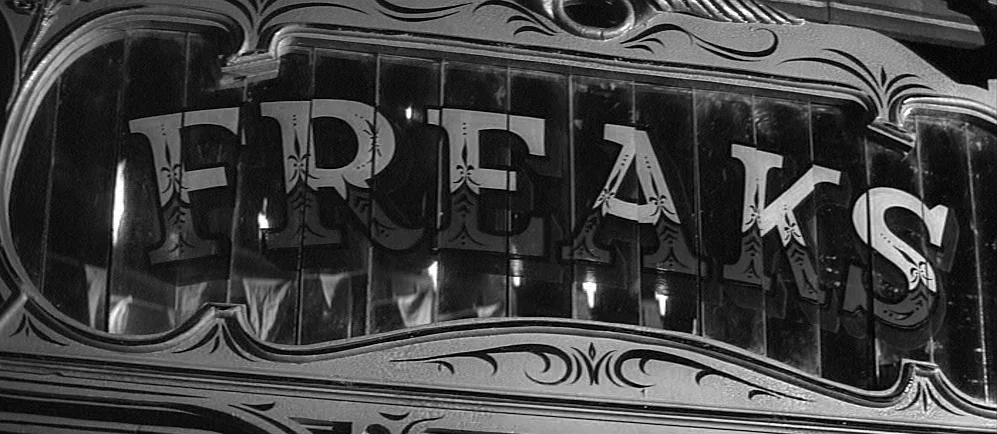 The Elephant Man (1980) movie still: closeup — A close view of an ornate, glass-paneled sign featuring the word Freaks in serif lettering. The sign…