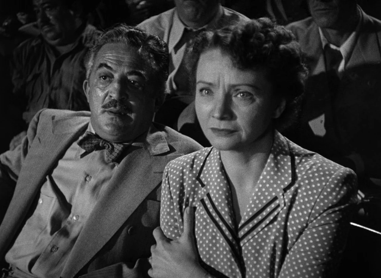 The Set-Up (1949) movie still: medium — A dark movie theater interior with rows of spectators in the background. A woman and a man sit together in…