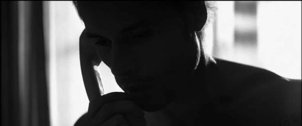 Memento (2000) movie still: closeup — An interior space is illuminated by a bright window behind a seated man. The man holds a plastic telephone…