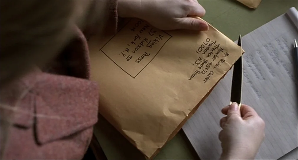 The Hurricane (1999) movie still: closeup — A workspace with a brown envelope addressed to Trenton State Prison on a desk. A hand uses a thin metal…
